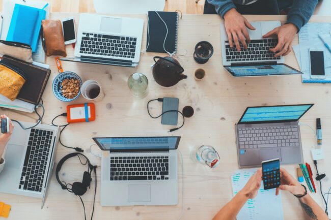 People sitting down near a table with laptop computers Busy table with different laptop computers
