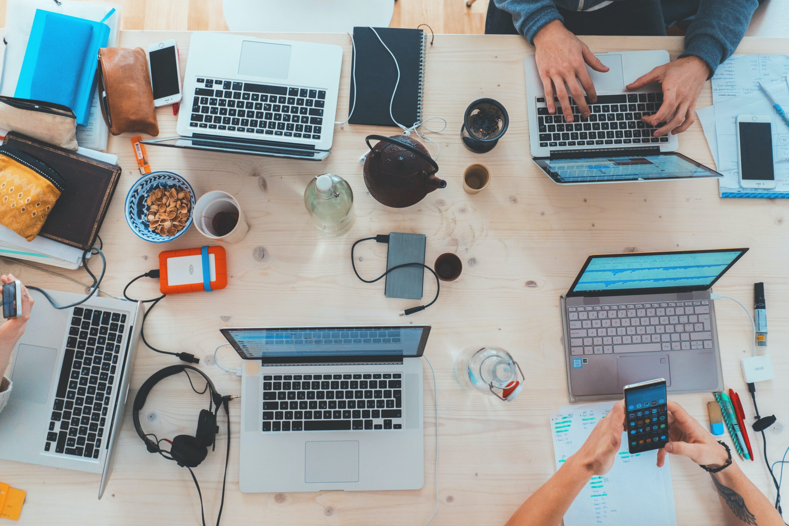 People sitting down near a table with laptop computers Busy table with different laptop computers
